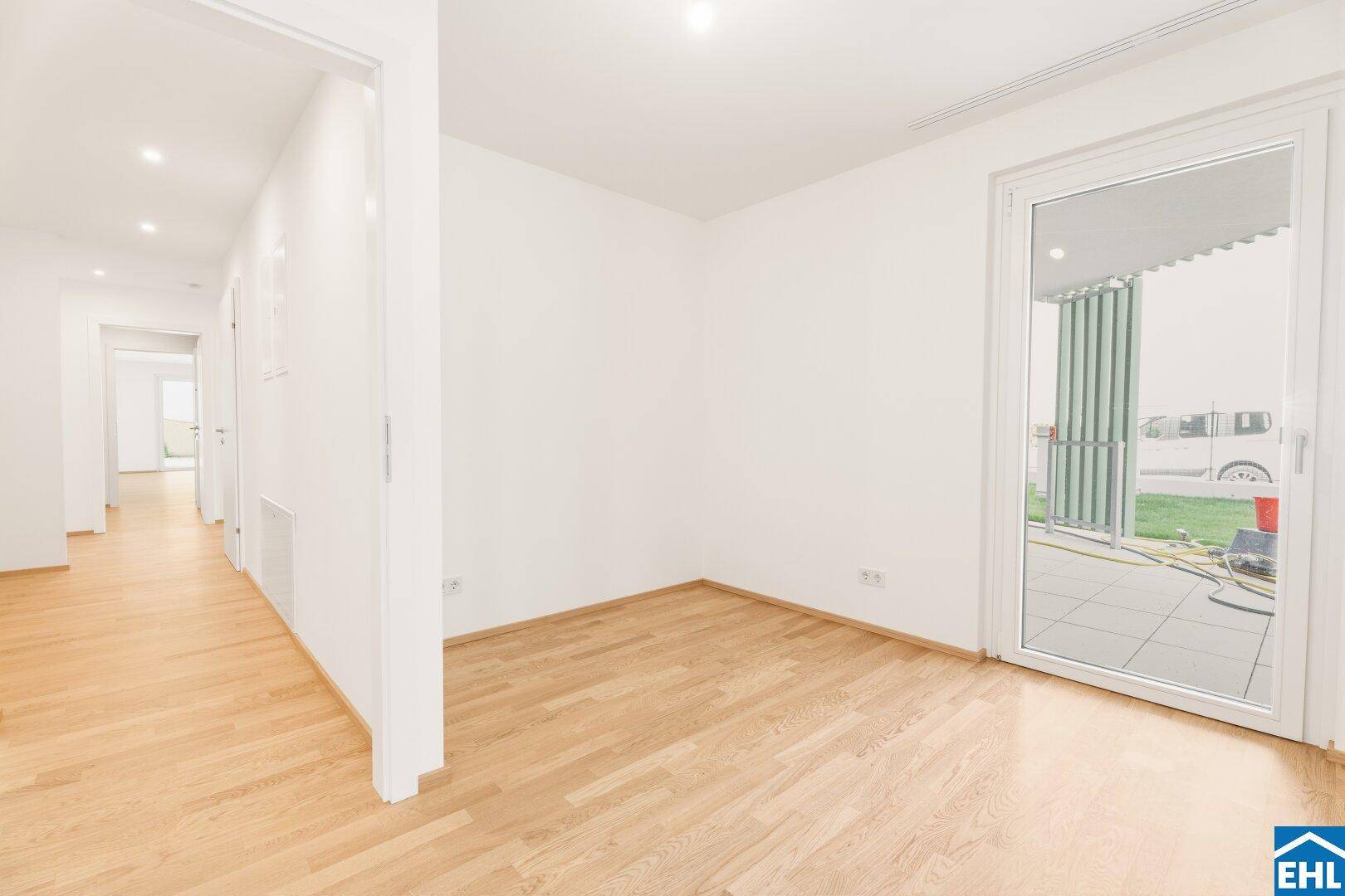 Heller Raum mit Parkettboden und Zugang zu einer Terrasse, angrenzend an einen Flur.