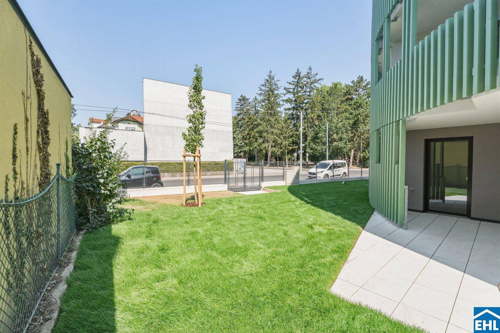 Kleiner Gartenbereich mit Rasen und Terrasse neben dem Gebäude, mit Blick auf die Straße.