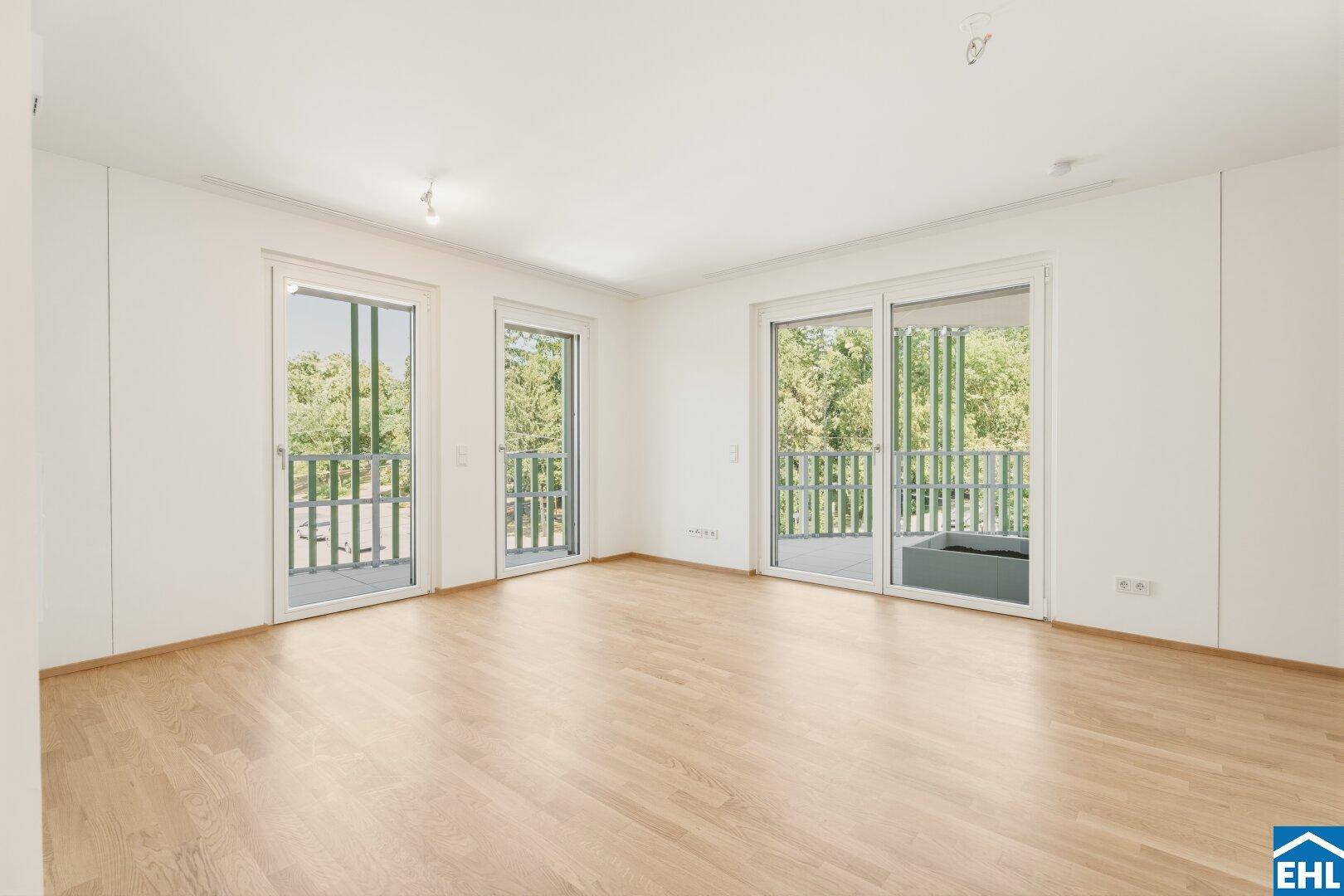 Lichtdurchflutetes Wohnzimmer mit hellem Parkettboden und mehreren Fenstertüren zu den Balkonen.