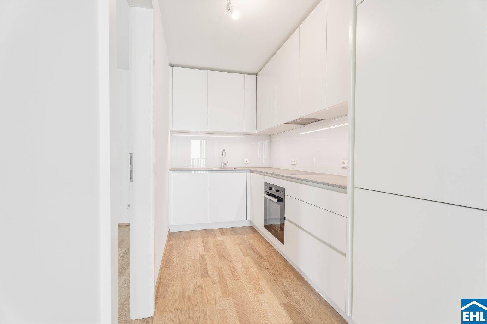 Moderne Einbauküche mit weißen Hochglanzfronten, integrierten Geräten und hellem Parkettboden.