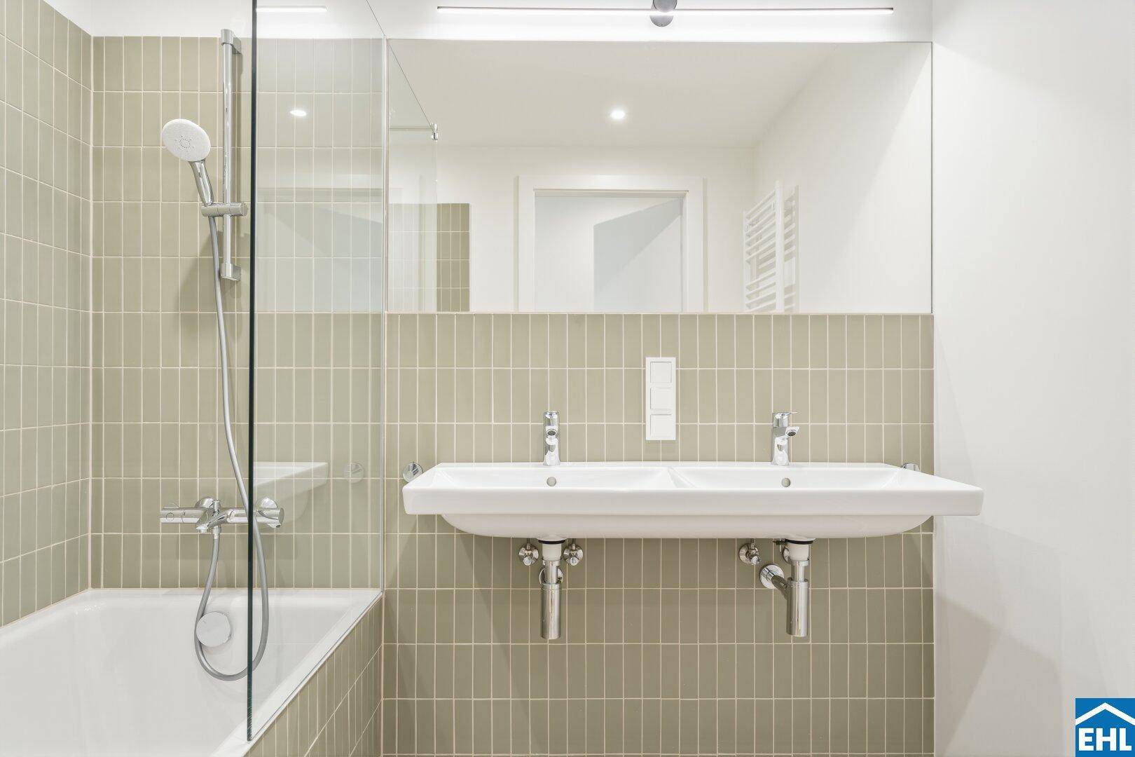 Modernes Badezimmer mit doppelten Waschbecken, Badewanne mit Dusche und beigefarbenen Fliesen.