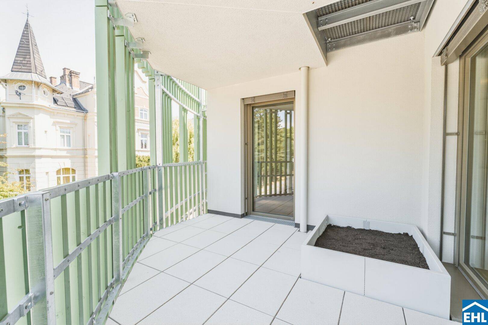 Geräumiger Balkon mit Fliesenboden, grünen Lamellen und Blick auf die Umgebung.