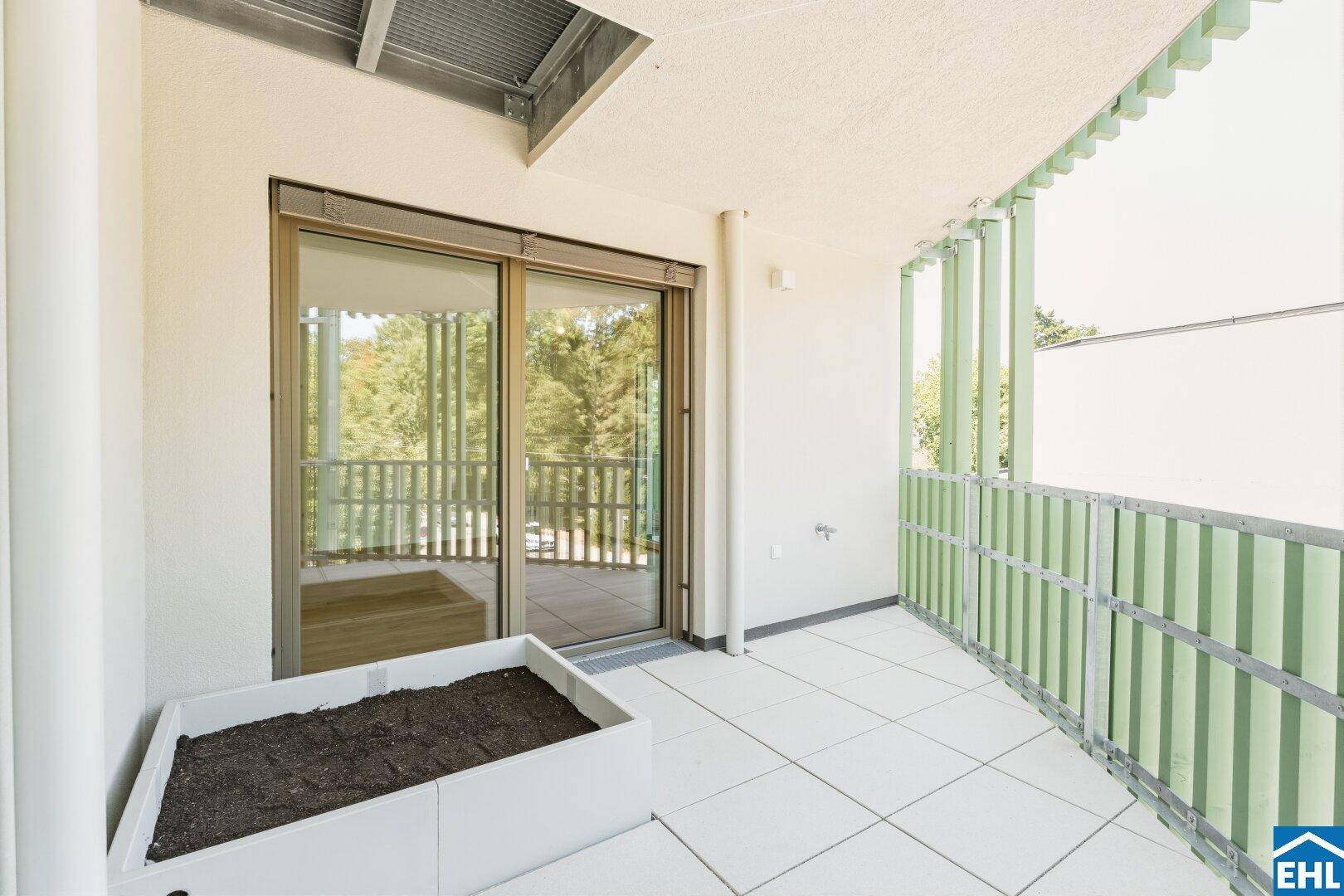 Heller Balkon mit Fliesenboden, Pflanzkasten und Zugang zum Innenbereich durch große Schiebetüren.