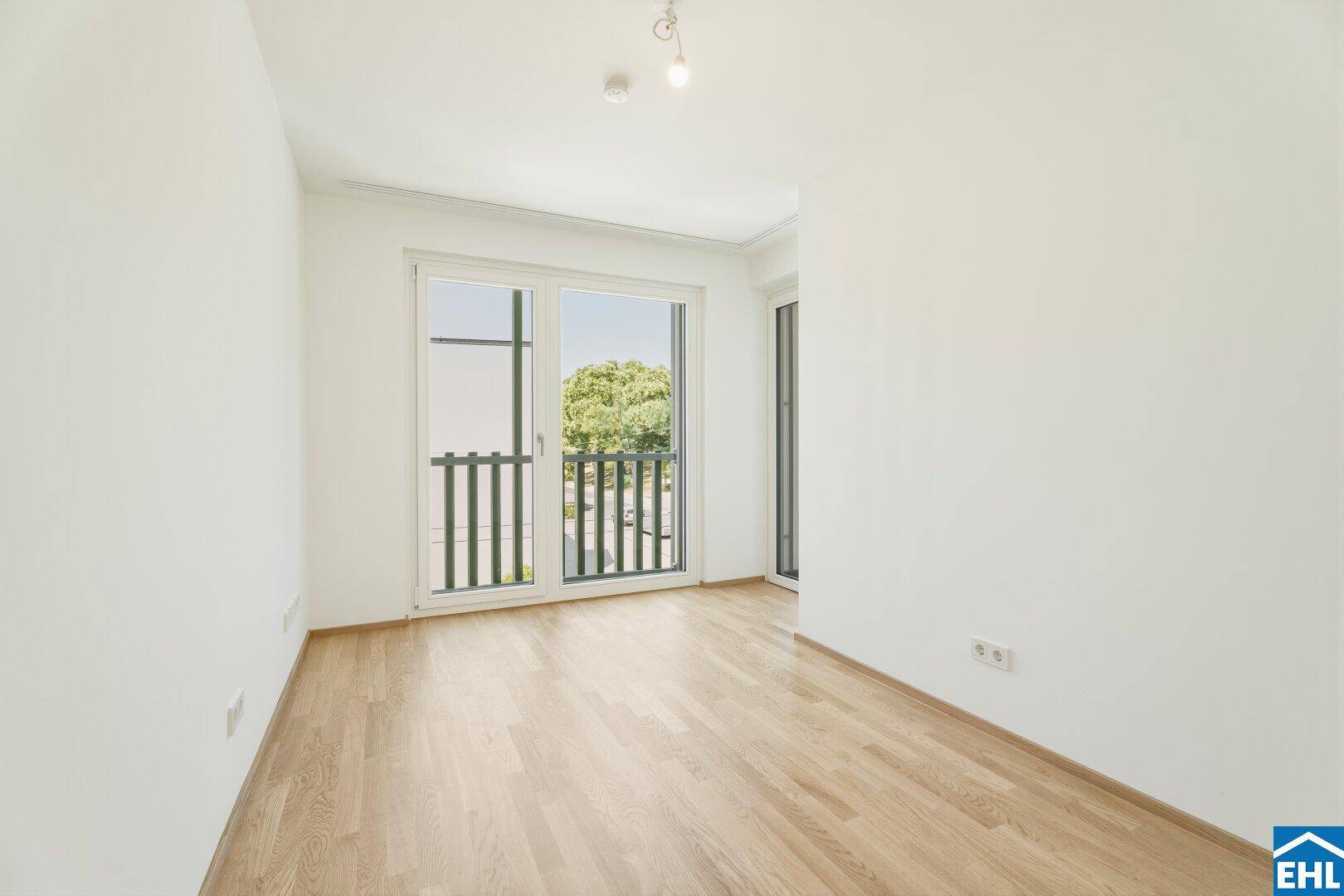 Helles Schlafzimmer mit Parkettboden und Zugang zu einem Balkon, bietet viel natürliches Licht.