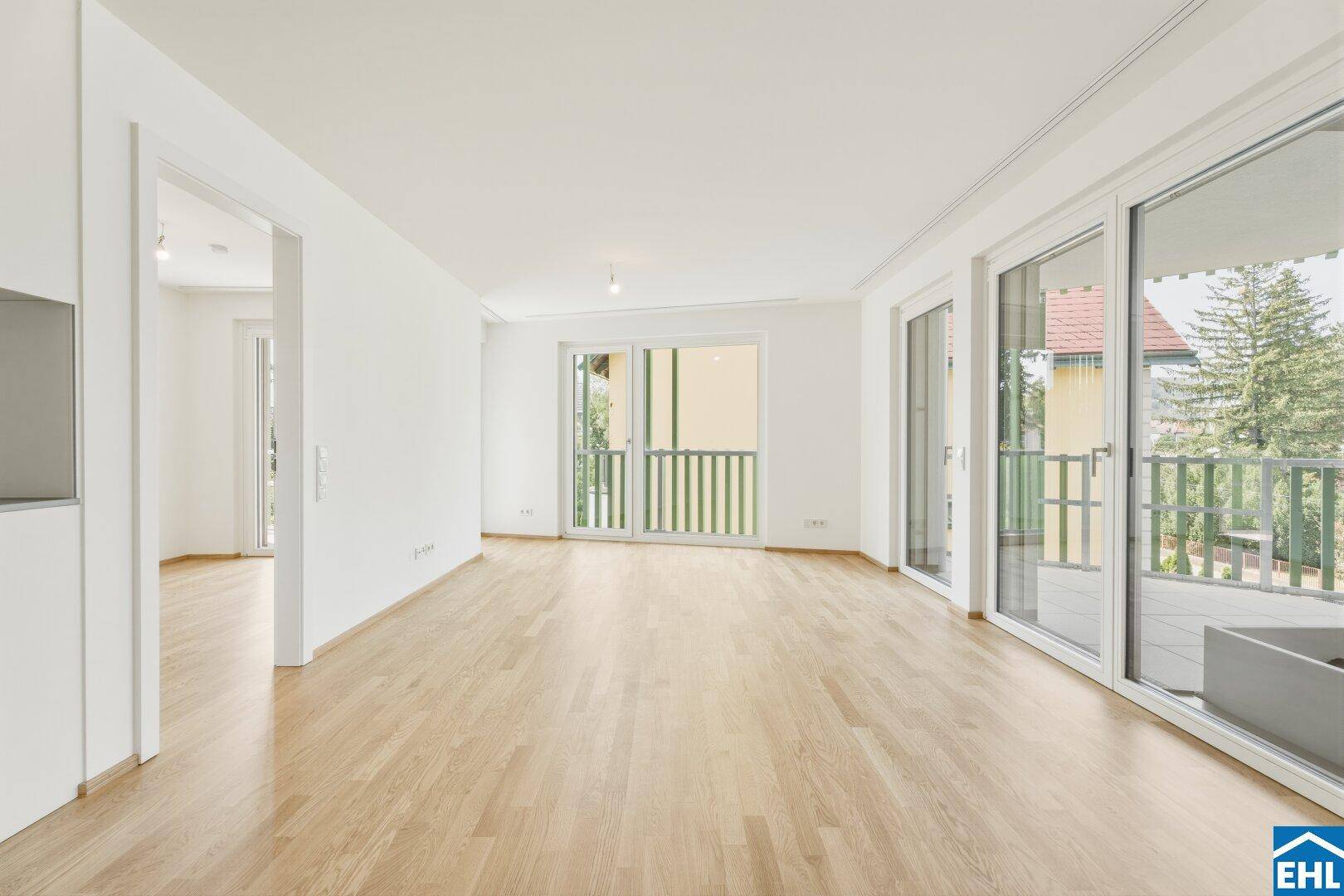 Geräumiges, helles Wohnzimmer mit hellem Parkettboden und Zugang zu einem Balkon.