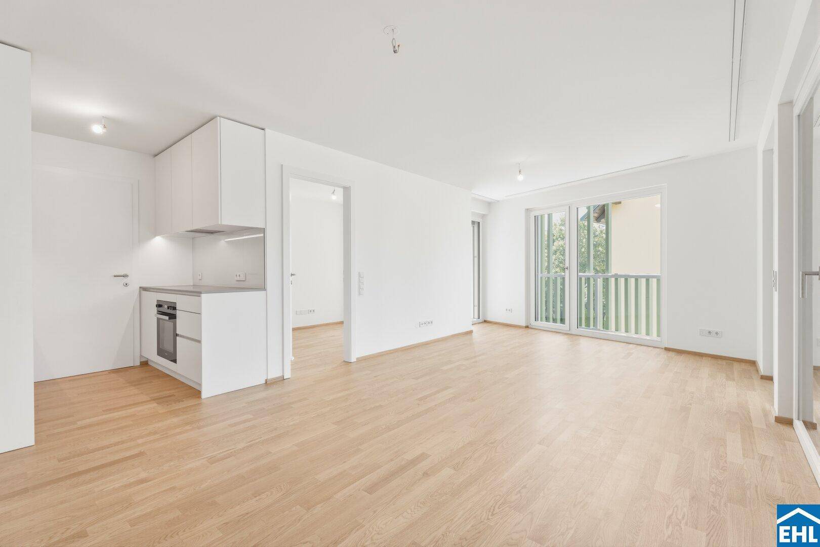 Heller Wohnbereich mit integrierter Küchenzeile, Parkettboden und Zugang zum Balkon.