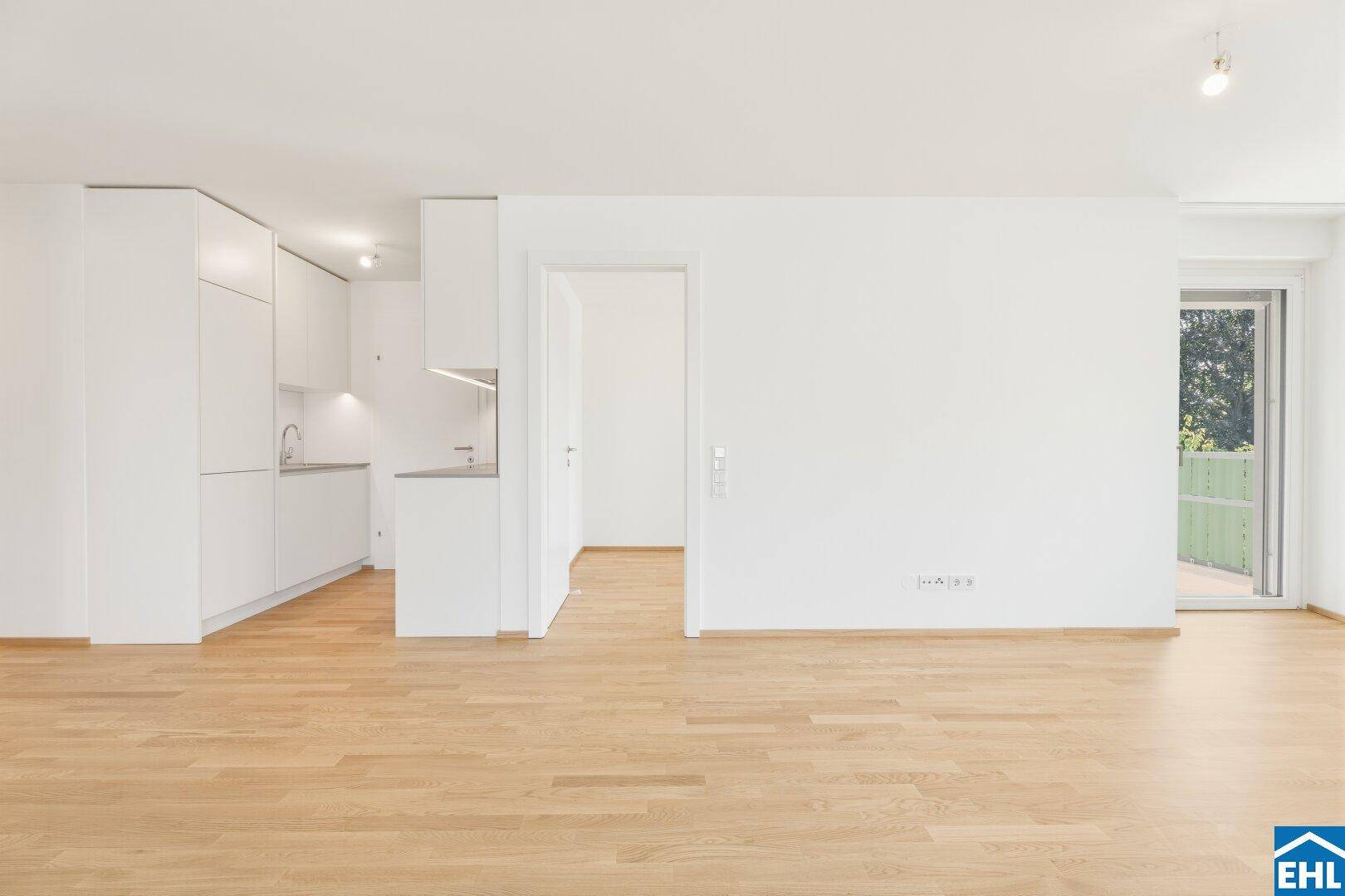 Moderne, weiße Küchenzeile im offenen Wohnbereich mit Parkettboden und viel Tageslicht.