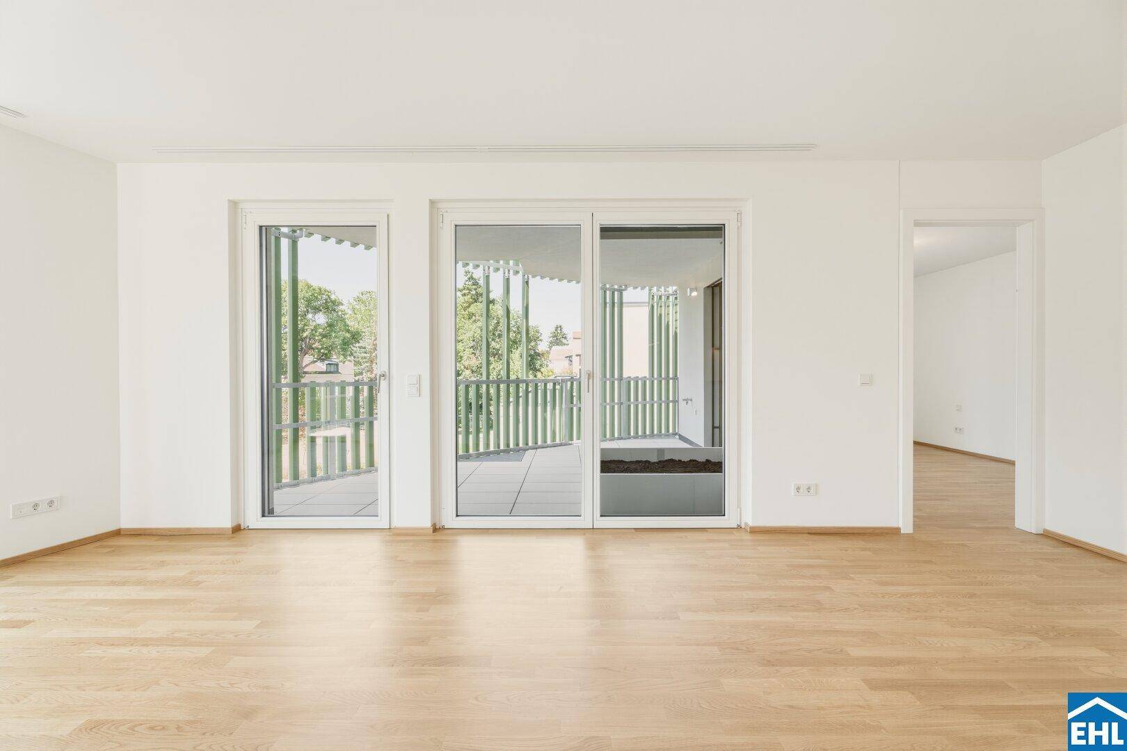 Heller Wohnraum mit großen Schiebetüren, die auf den Balkon führen und viel Licht hereinlassen.