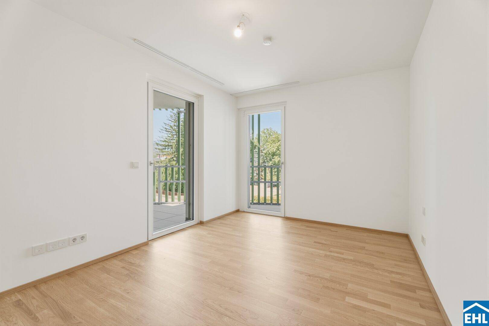 Helles Schlafzimmer mit zwei Balkonzugängen und Parkettboden, bietet viel natürliches Licht.