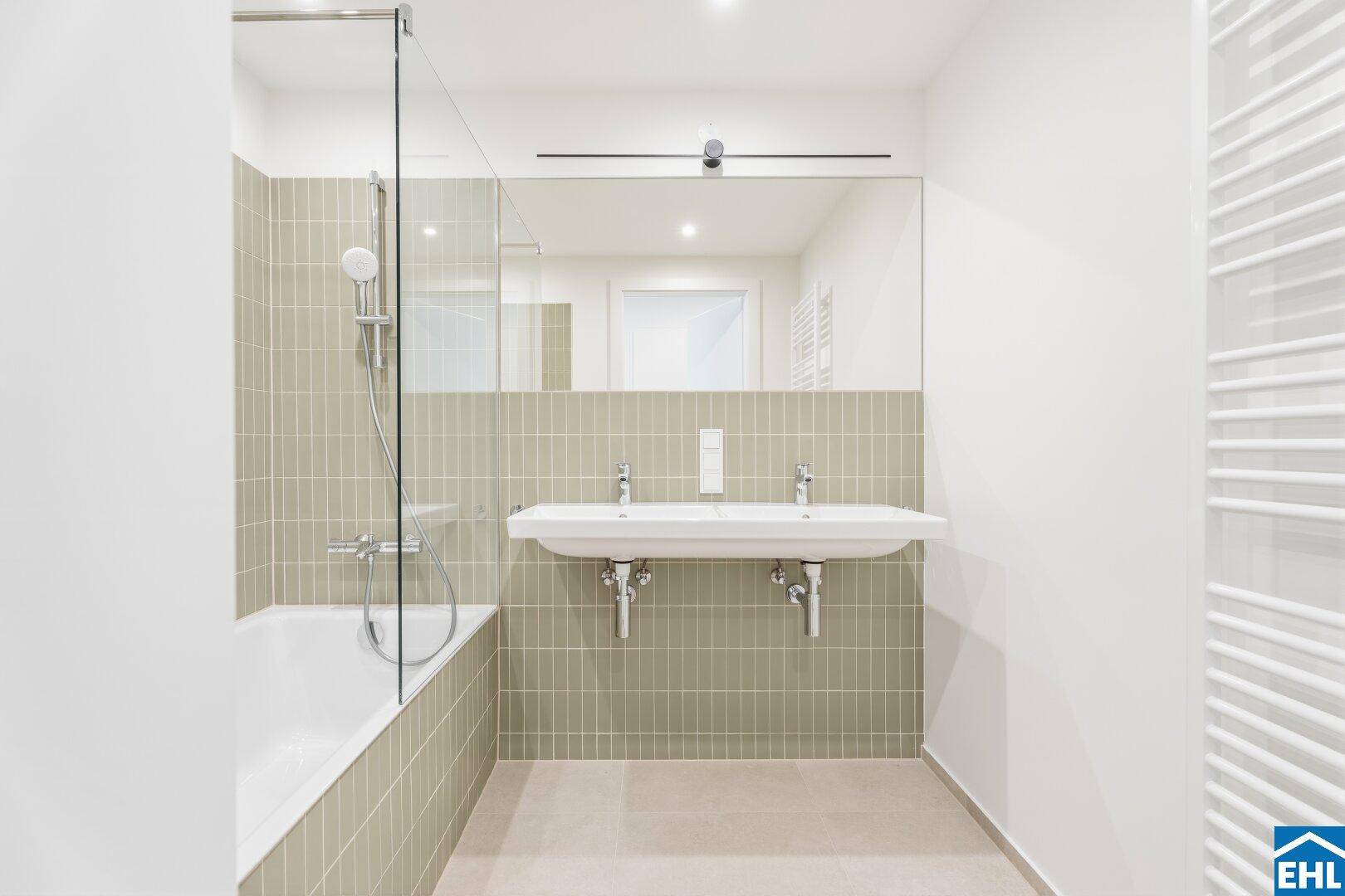 Modernes Badezimmer mit Badewanne, Duschwand, Doppelwaschbecken und beheiztem Handtuchhalter.