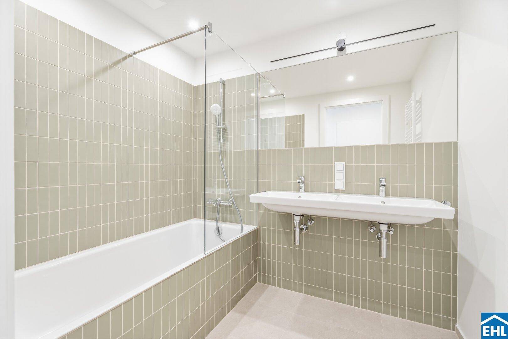 Helles Badezimmer mit Badewanne, Glasduschwand, Doppelwaschbecken und modernen Fliesen.