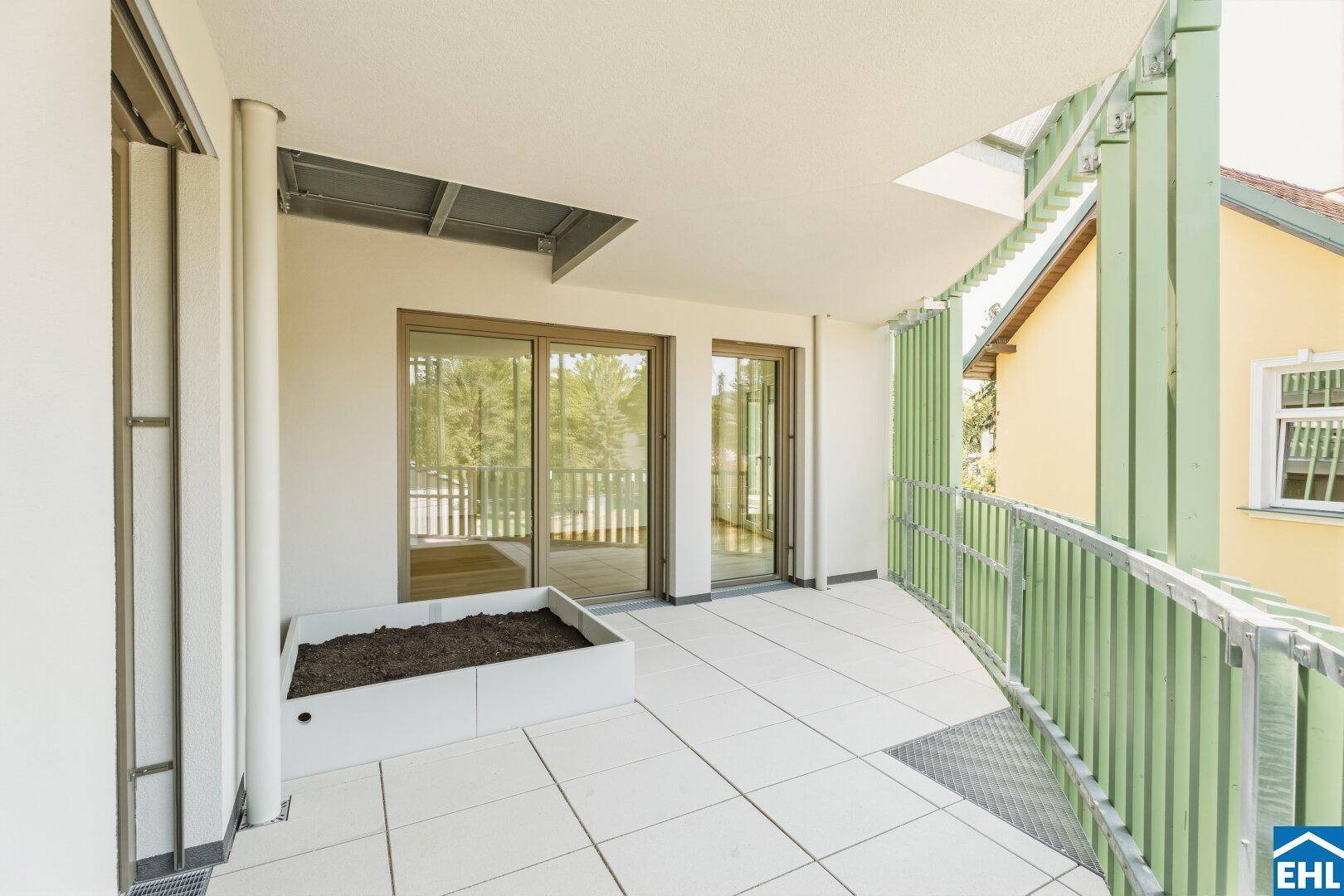 Großer Balkon mit Fliesenboden, Pflanzkasten und grünen Geländern, bietet viel Platz im Freien.