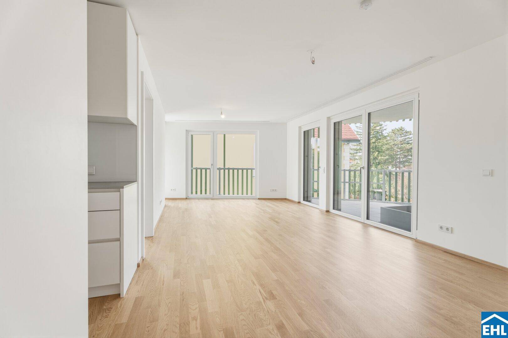 Heller Wohnbereich mit integrierter Küchenzeile, Parkettboden und Zugang zu einem Balkon.