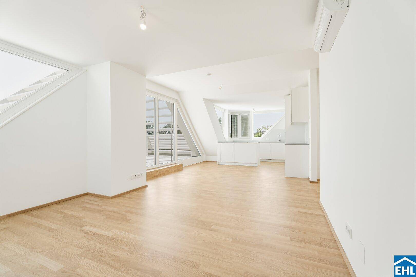 Offener Wohn- und Küchenbereich mit Holzboden, großen Fenstern und moderner Einbauküche.