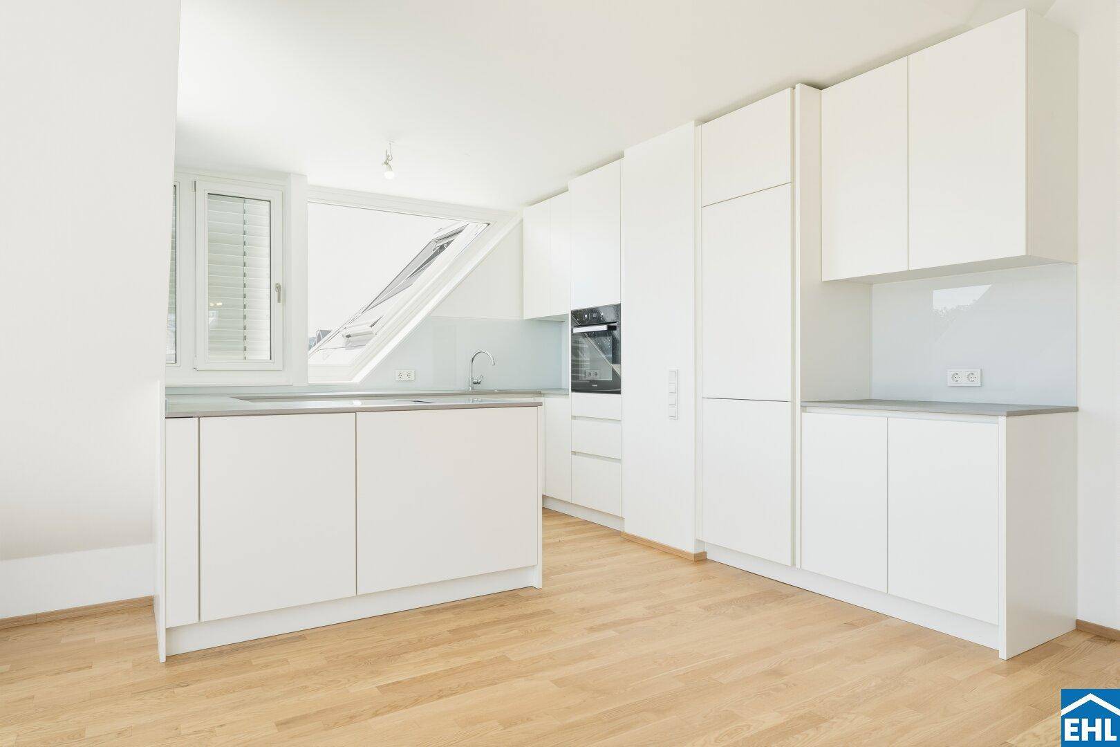 Moderne weiße Einbauküche mit integriertem Backofen, Spüle und einem Dachfenster für viel Licht.