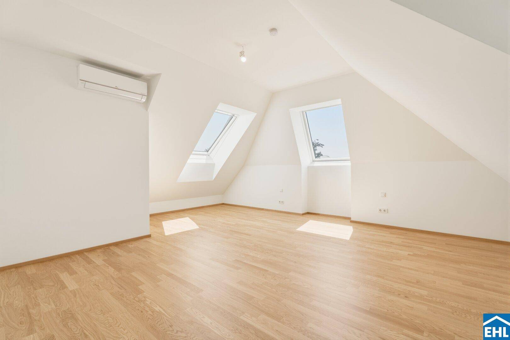 Helles Schlafzimmer im Dachgeschoss mit Holzboden, Klimaanlage und zwei Dachfenstern.