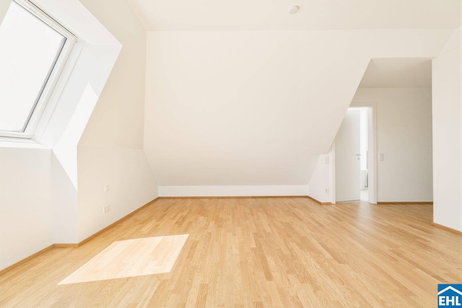Geräumiges Zimmer mit Holzboden, Dachschräge und einem großen Dachfenster, das viel Licht spendet.