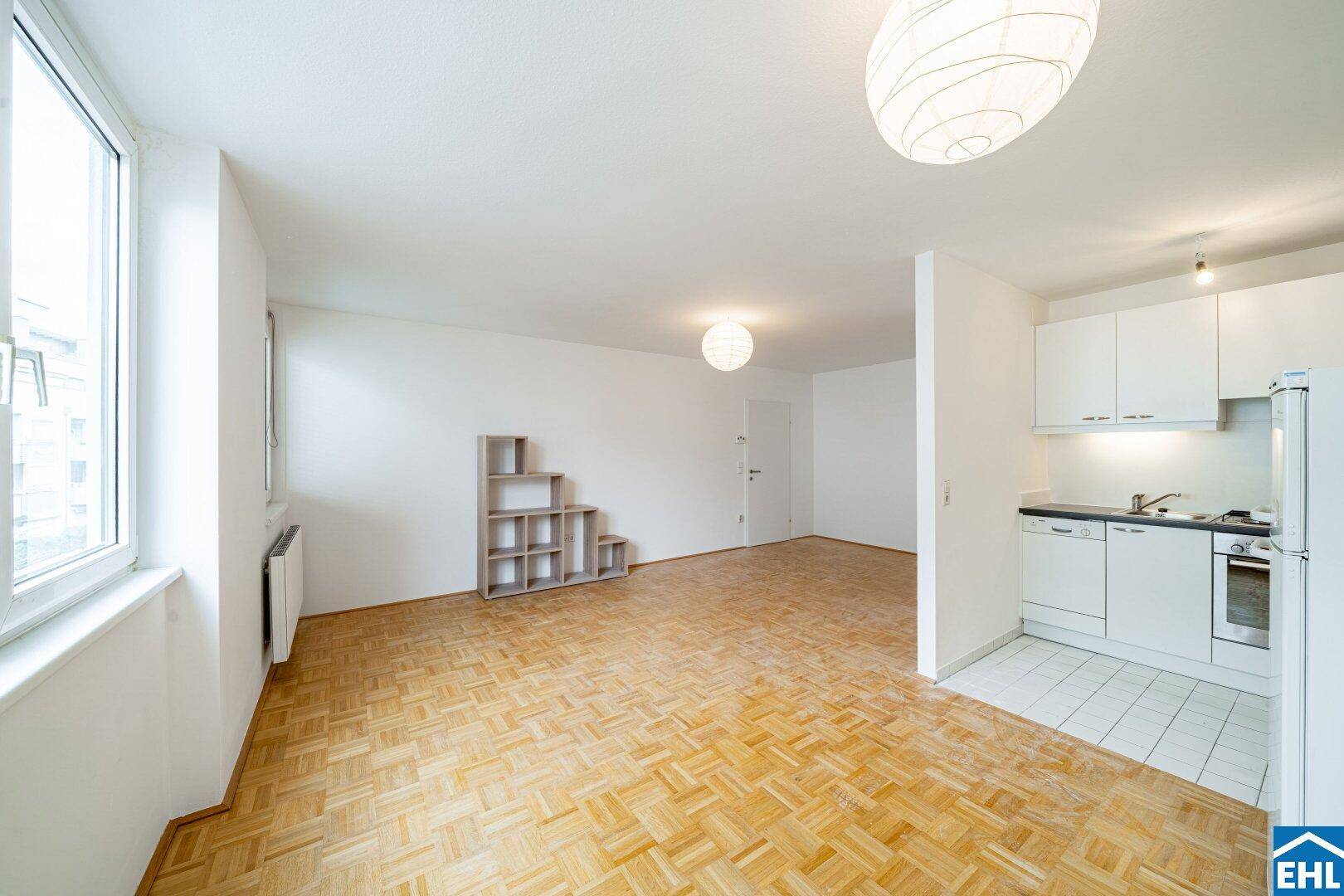 Geräumiger Wohnbereich mit Parkettboden, großen Fenstern und integrierter Küchenzeile.