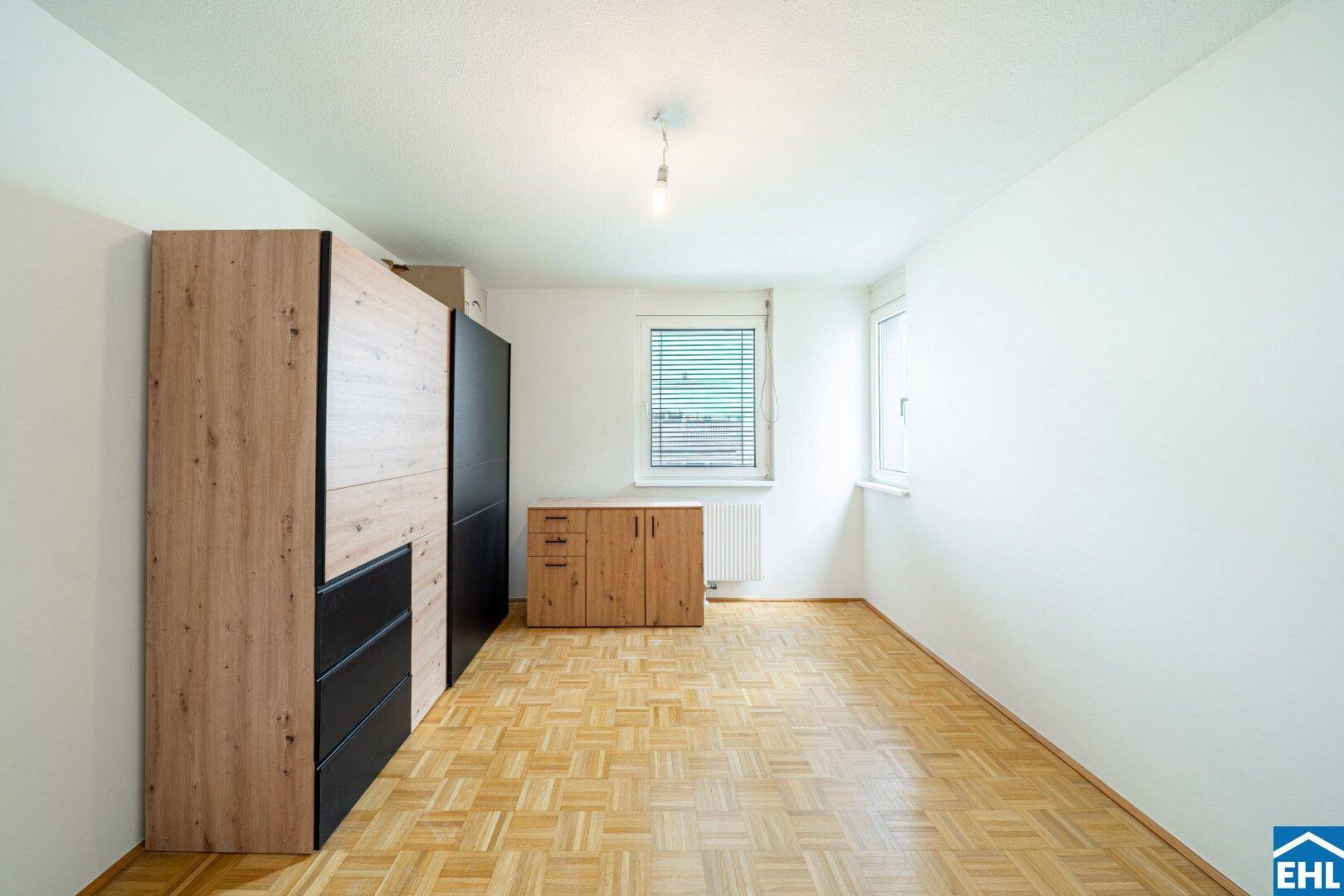 Schlafzimmer mit Parkettboden, Fenster und modernen Holz-Schwarz-Schränken.