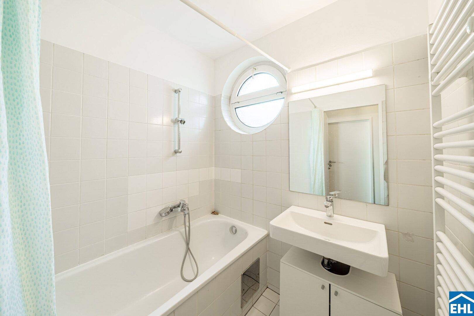 Modernes Badezimmer mit Badewanne, Waschbecken, Spiegel und charakteristischem Rundfenster.