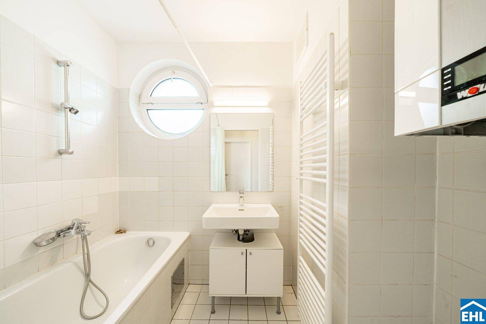 Helles Badezimmer mit Badewanne, Waschbecken, Handtuchheizkörper und Boiler an der Wand.