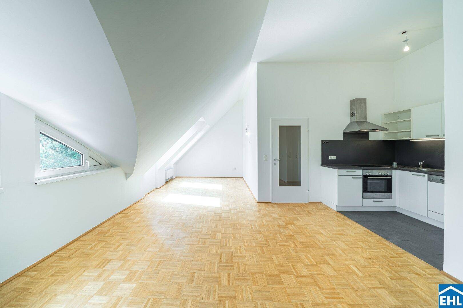 Offener Wohnbereich im Dachgeschoss mit integrierter Küchenzeile, Parkettboden und schrägen Wänden.
