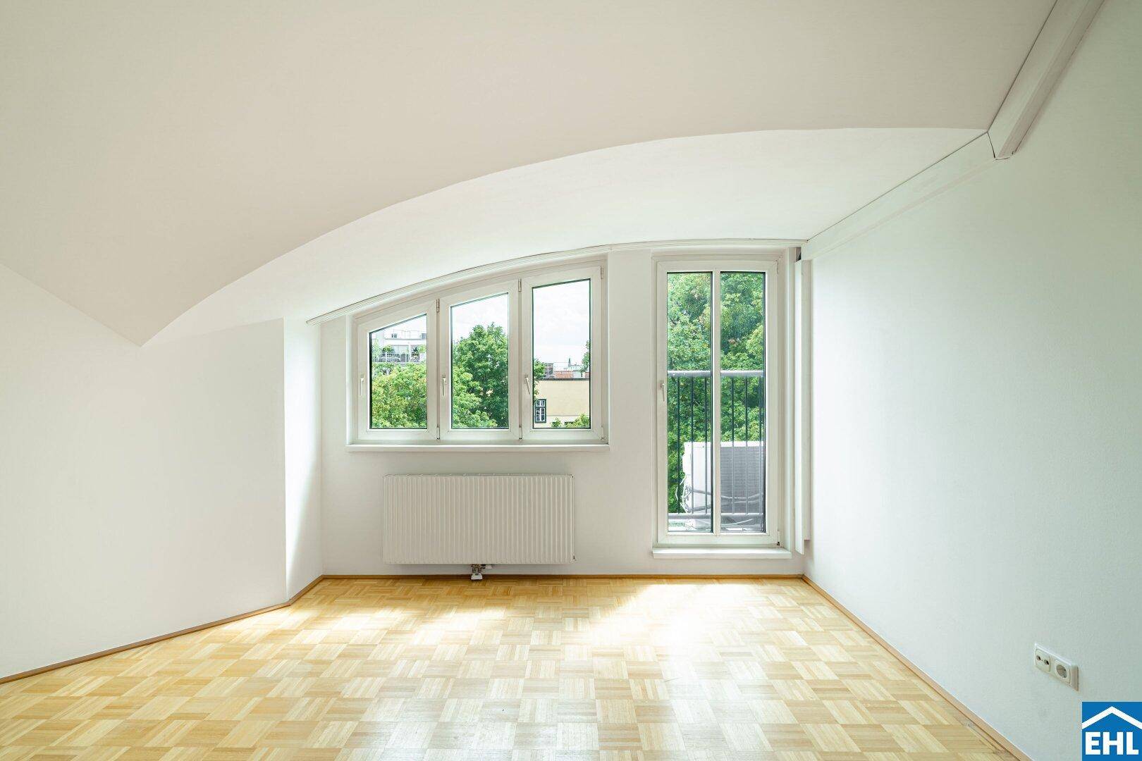 Heller Raum mit Parkettboden, schrägen Wänden und Fenstern, die viel Tageslicht hereinlassen.