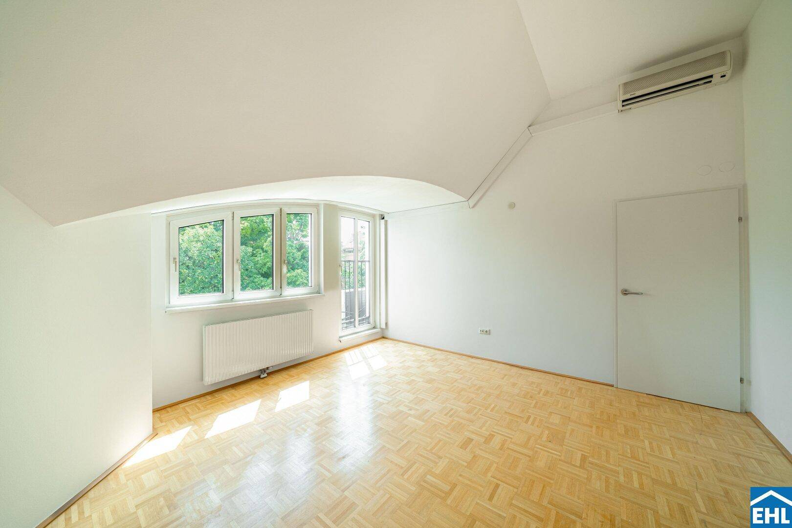 Geräumiges Zimmer im Dachgeschoss mit Parkettboden, Klimaanlage und Zugang zu einem französischen Balkon.