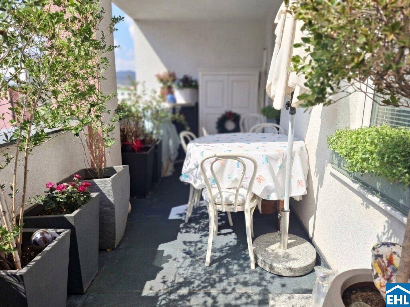 Sonniger Balkon mit Esstisch, Sonnenschirm und vielen Pflanzen für Mahlzeiten im Freien.
