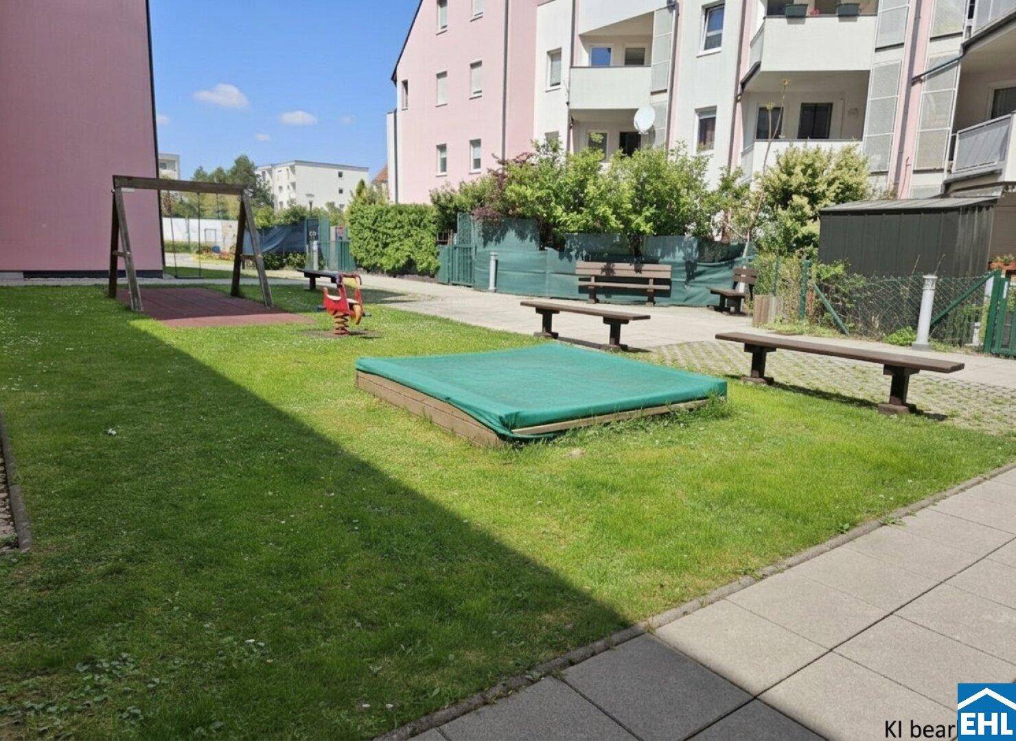 Gemeinschaftsgarten mit Spielplatz, Sandkasten und Bänken für Kinder und Familien.