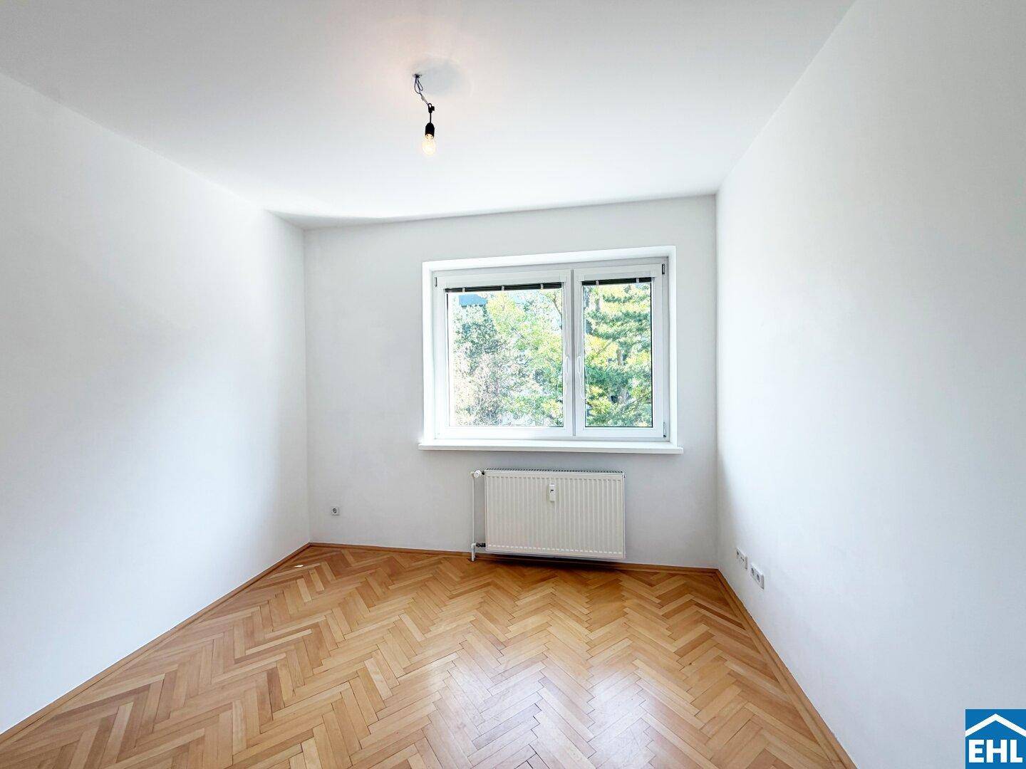 Helles Schlafzimmer mit klassischem Fischgrätparkett und Blick ins Grüne durch das Fenster.