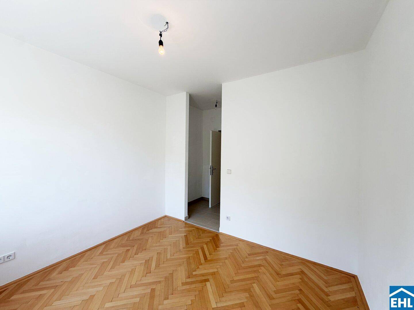 Geräumiges Zimmer mit Fischgrätparkett und Zugang zu einem Flur, ideal für flexible Nutzung.