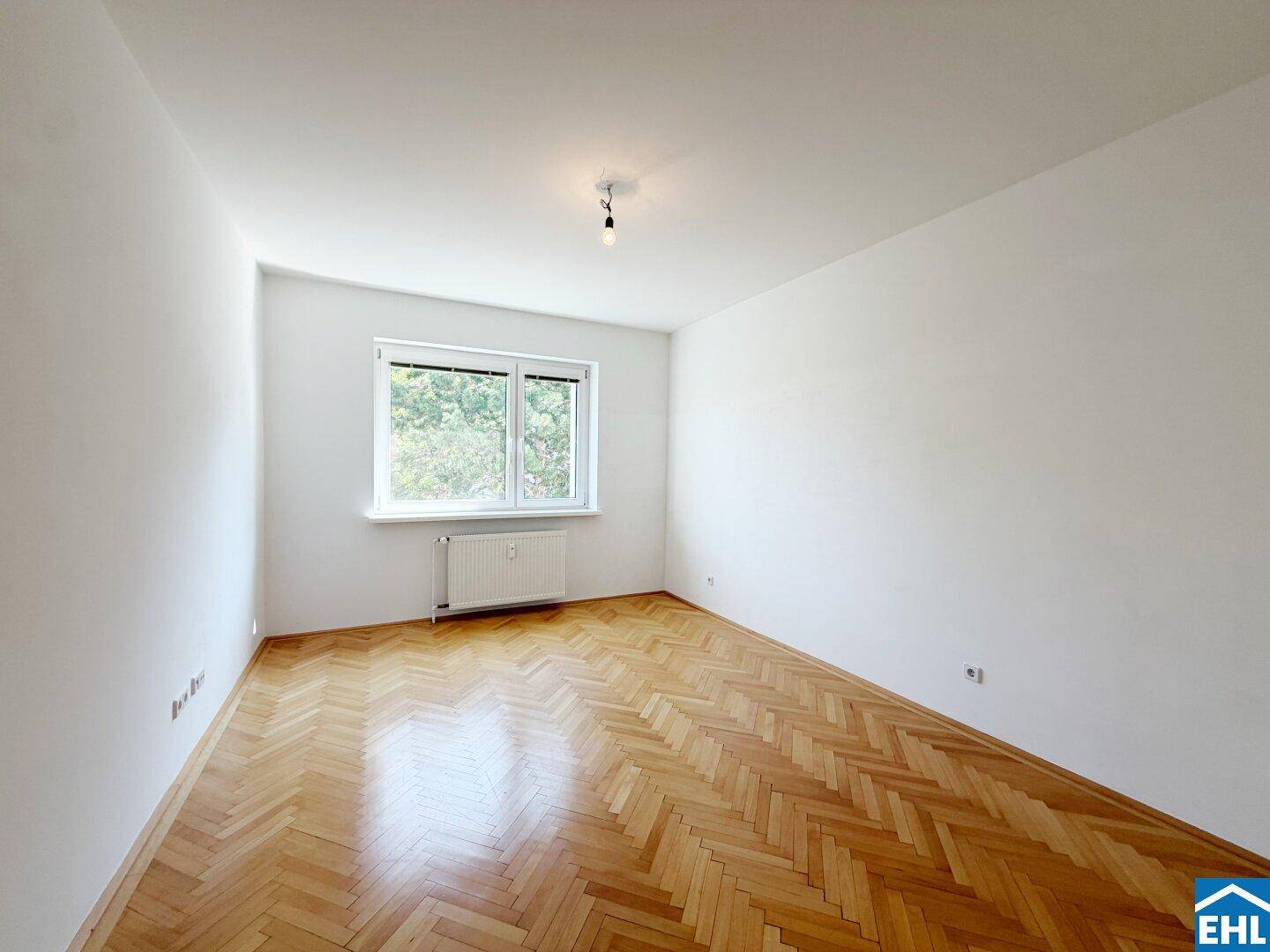 Lichtdurchflutetes Schlafzimmer mit Fischgrätparkett und einem Fenster mit Ausblick ins Grüne.