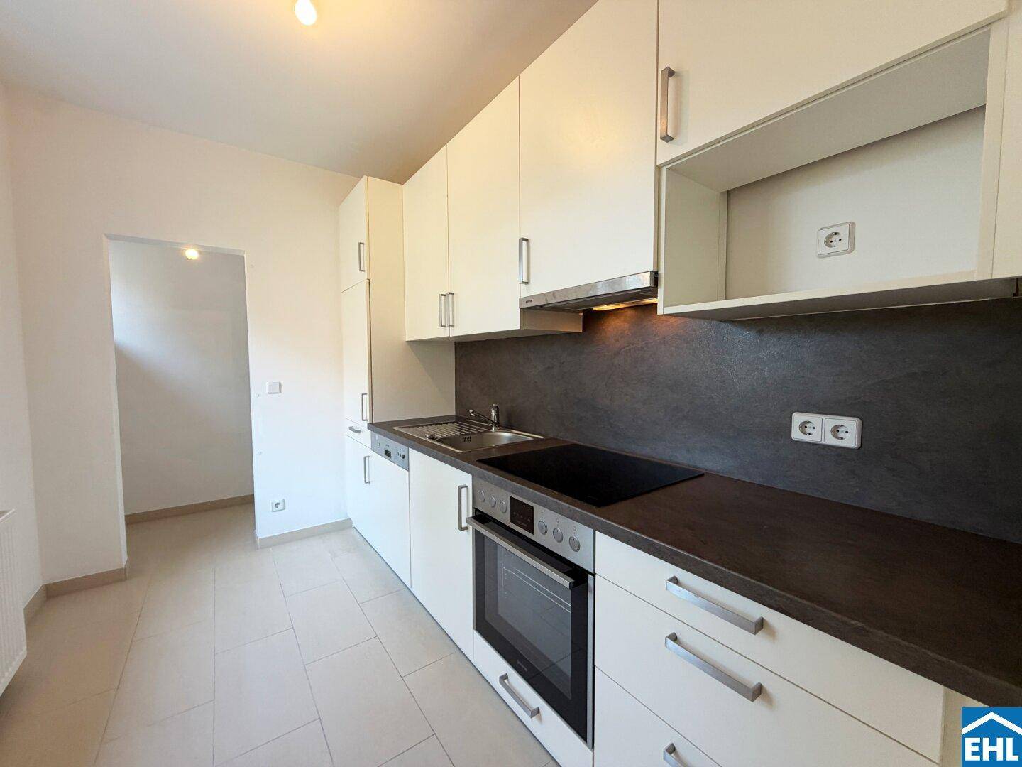 Moderne Einbauküche mit weißen Schränken, dunklen Arbeitsplatten und integrierten Geräten.