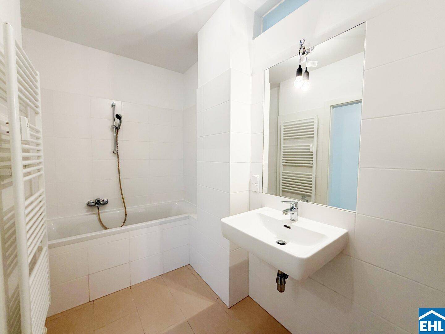 Modernes Badezimmer mit weißen Fliesen, Badewanne, Waschbecken und beheiztem Handtuchhalter.