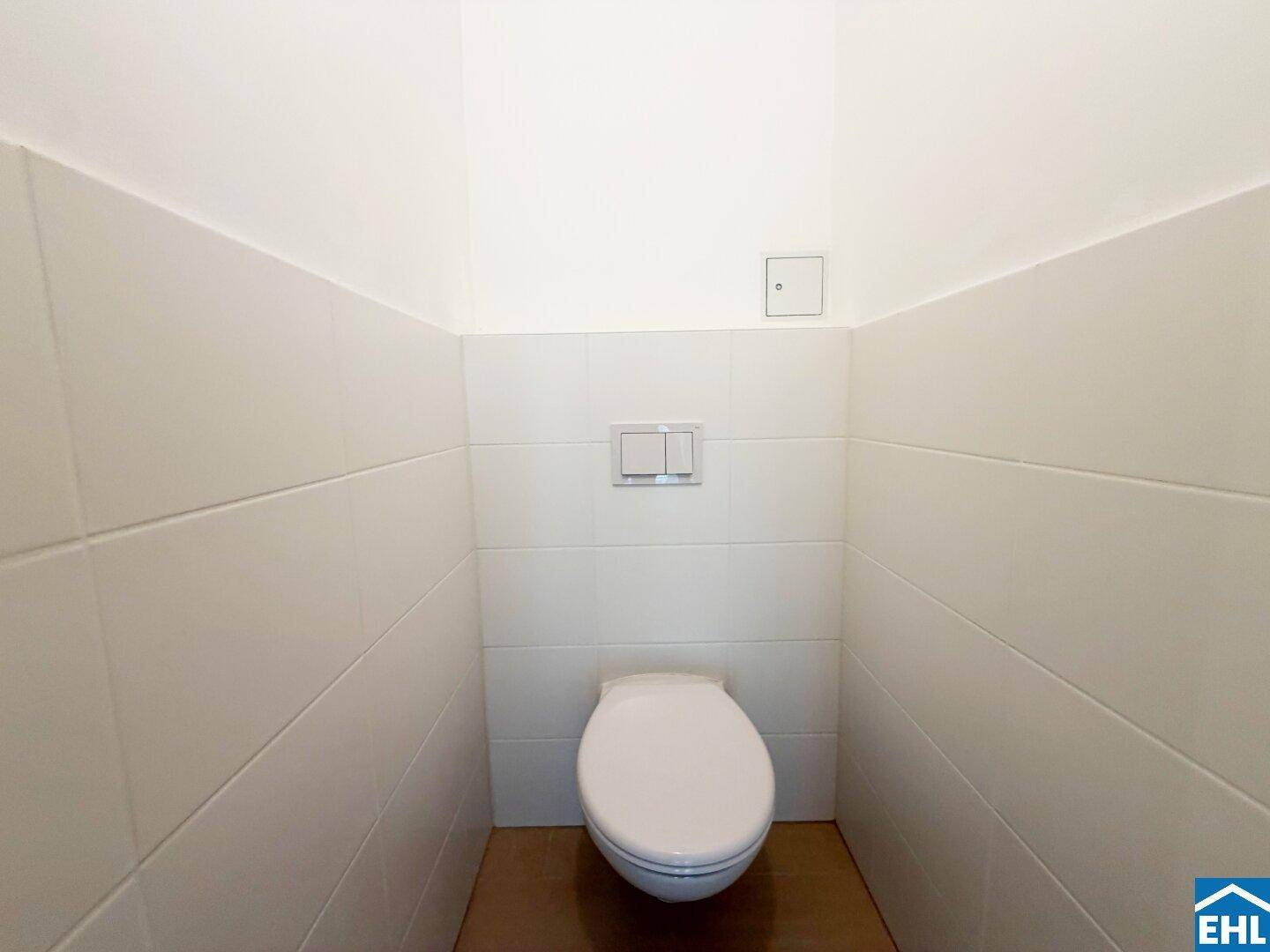 Separates WC mit wandhängender Toilette und weißen Fliesen, sauber und funktional.