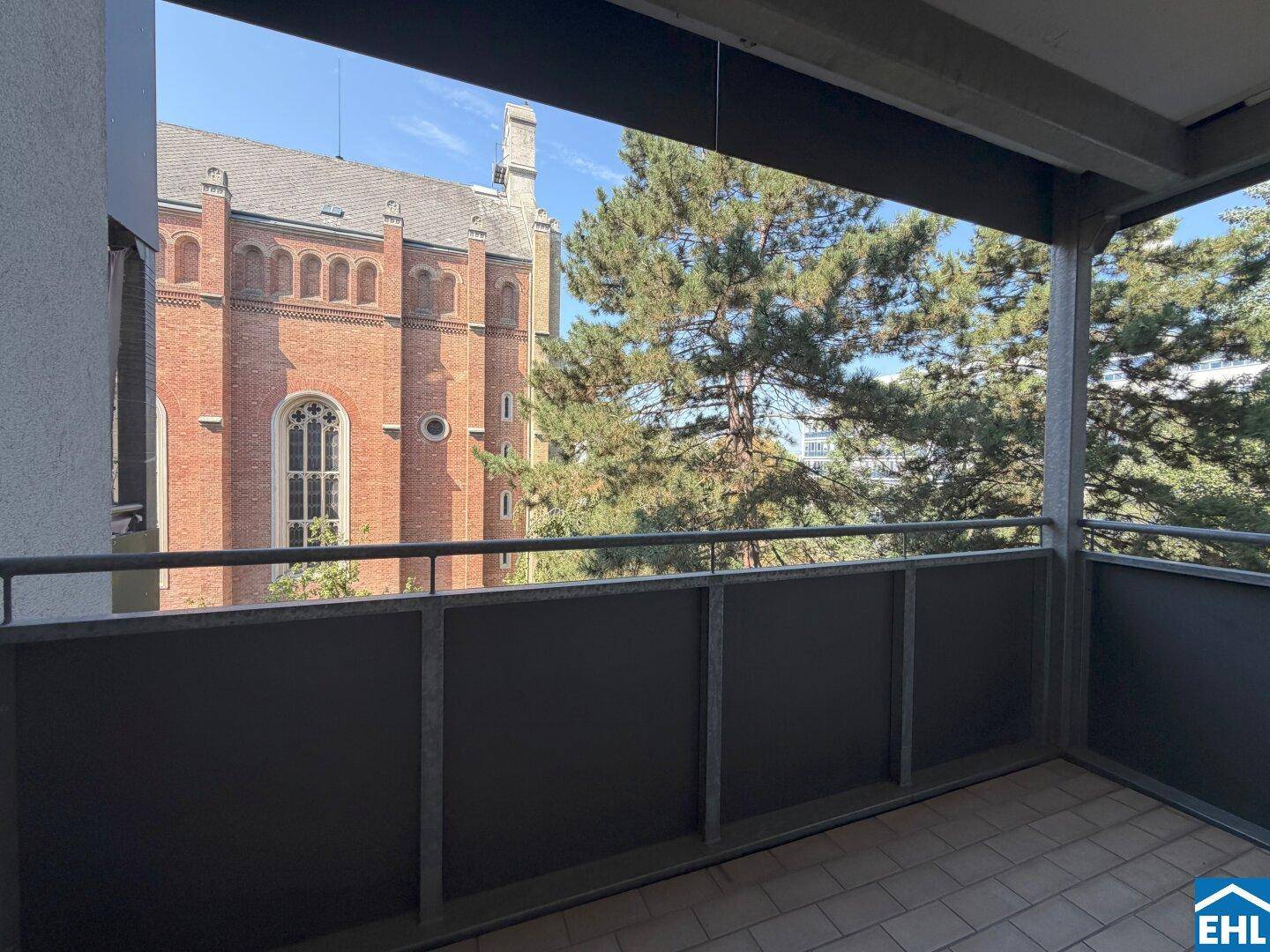 Balkon mit Fliesenboden und malerischem Blick auf ein historisches Backsteingebäude und Bäume.