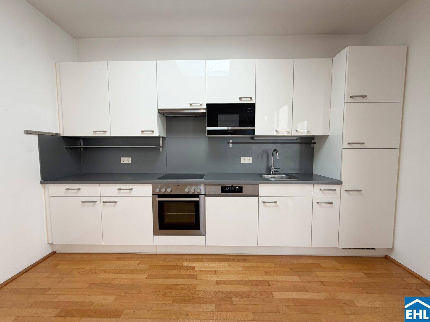 Moderne Einbauküche mit weißen Hochglanzfronten, integrierten Geräten und dunkler Arbeitsplatte.