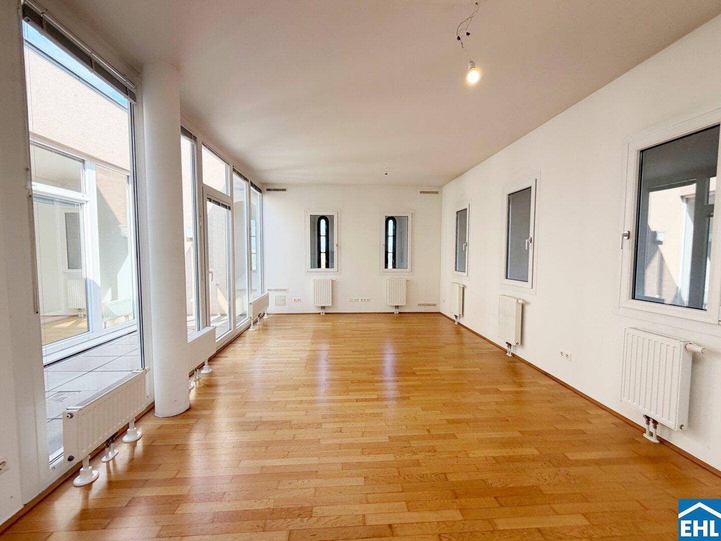 Geräumiges Wohnzimmer mit Parkettboden, hohen Decken und großen Fenstern, die viel Licht hereinlassen.