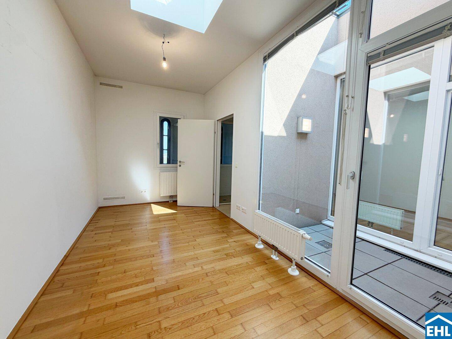 Helles Zimmer mit Parkettboden, Oberlicht und Zugang zu einem privaten Außenbereich.