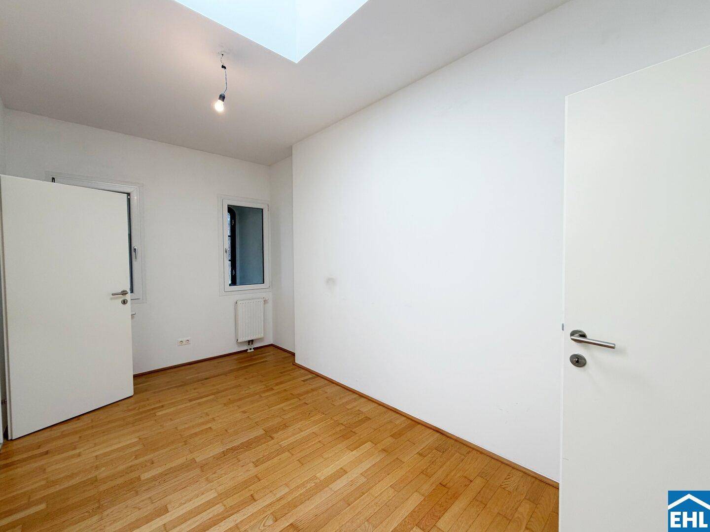 Leeres Zimmer mit Parkettboden, weiß gestrichenen Wänden und einem Oberlicht.