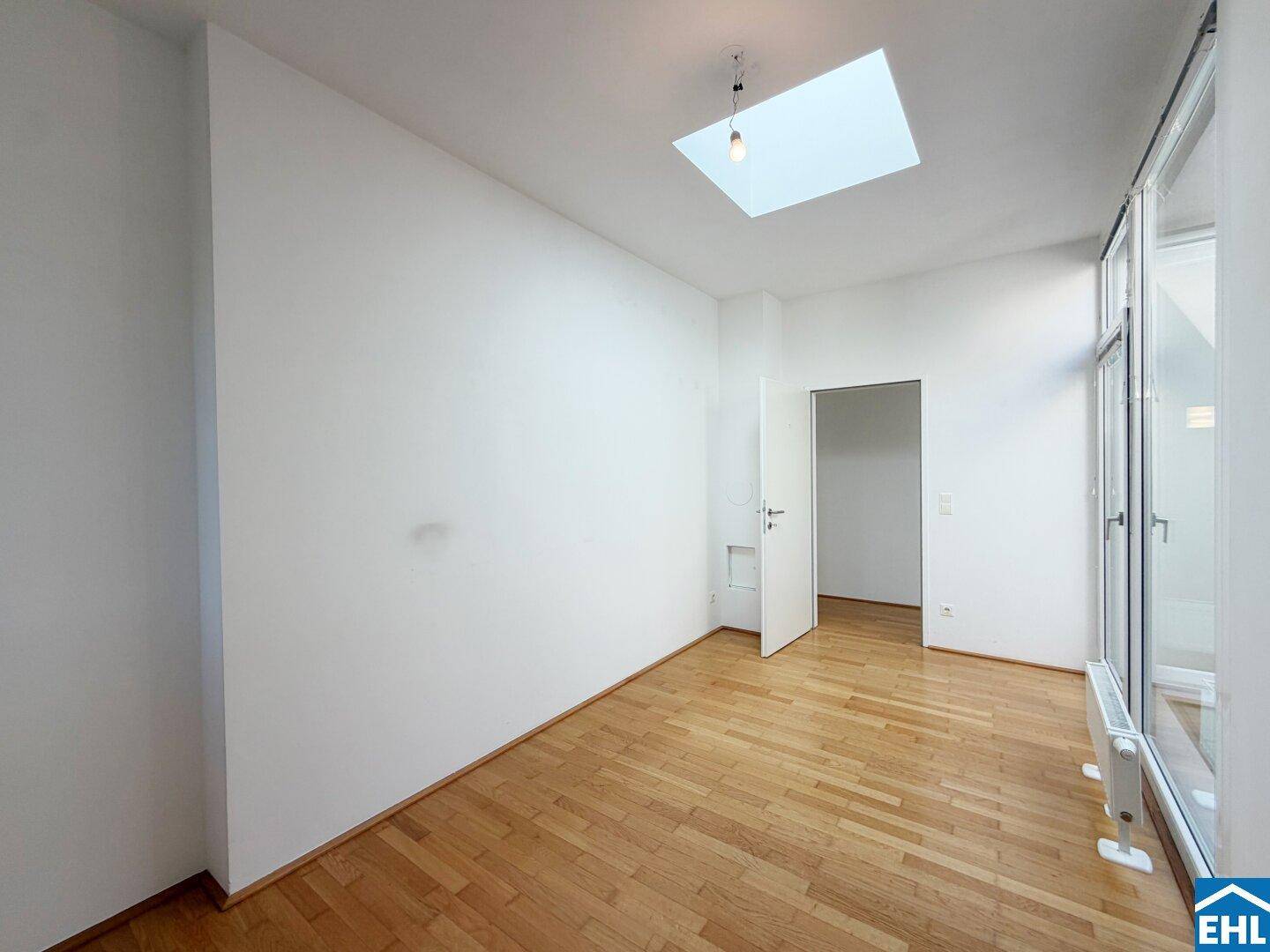Geräumiges Zimmer mit Parkettboden, Oberlicht und einer Tür, die zu einem weiteren Raum führt.