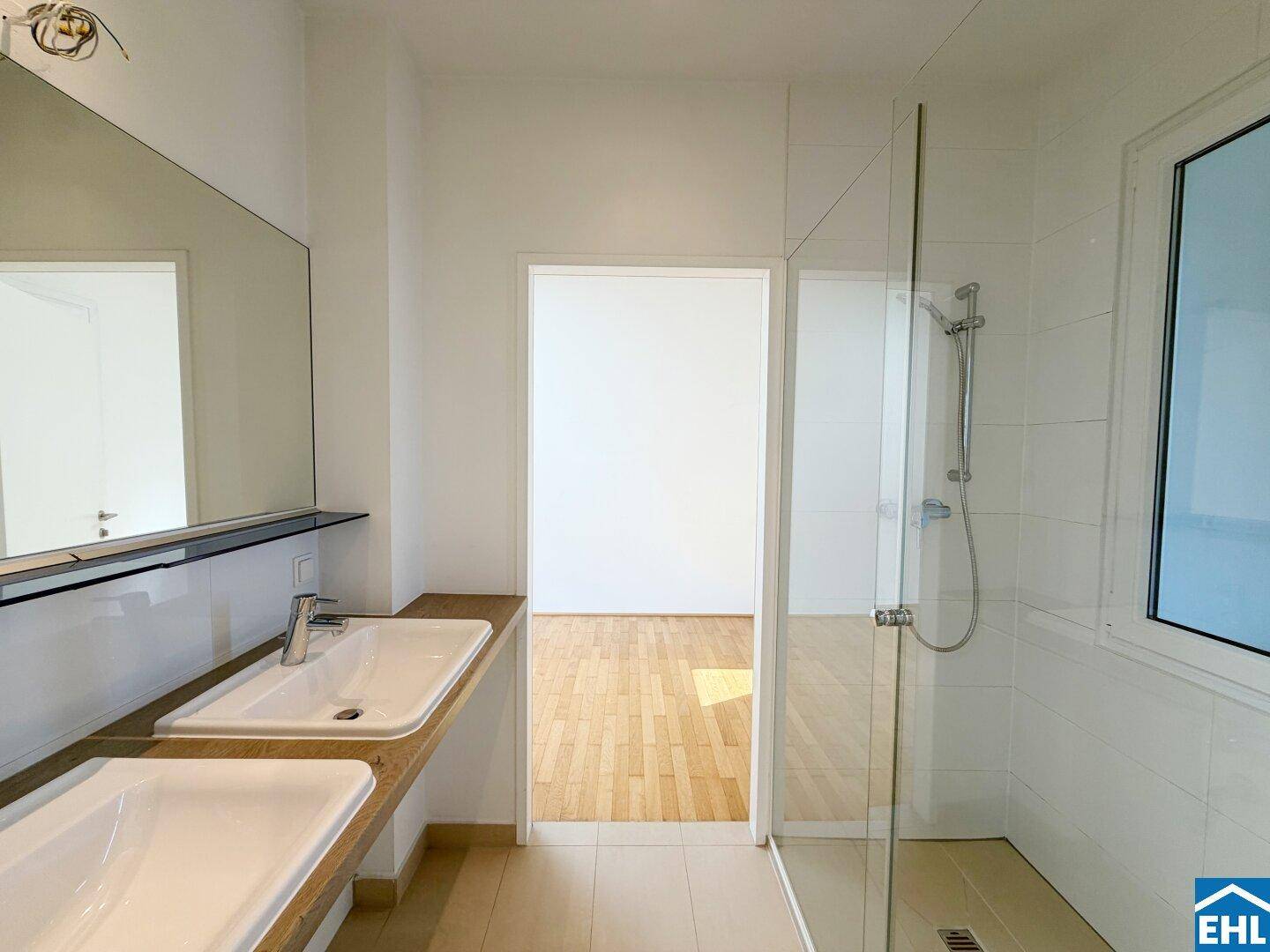 Modernes Badezimmer mit zwei Waschbecken, Duschkabine und Fenster für Tageslicht.