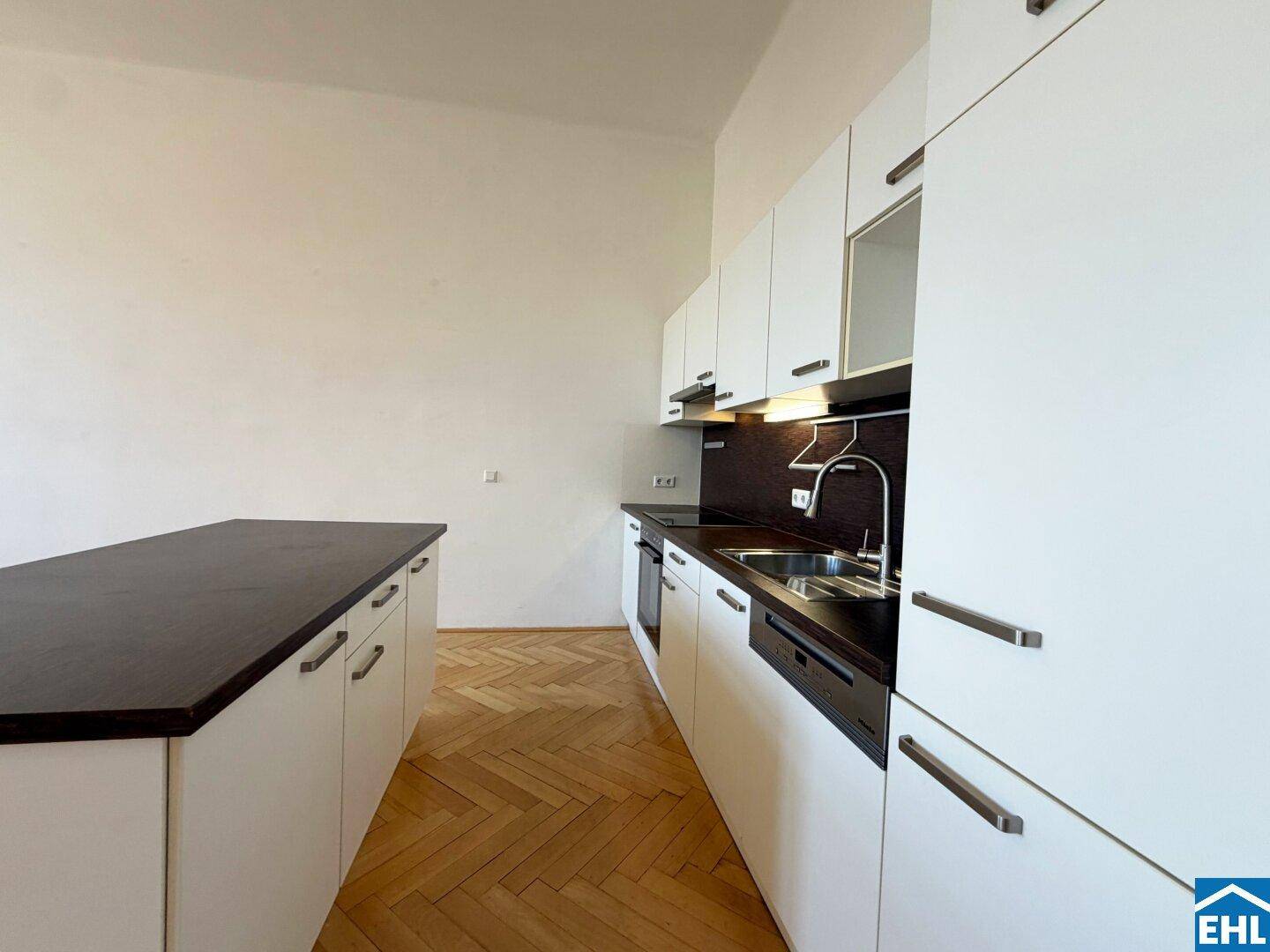 Moderne Einbauküche mit weißen Schränken, dunkler Arbeitsplatte und integrierten Geräten.