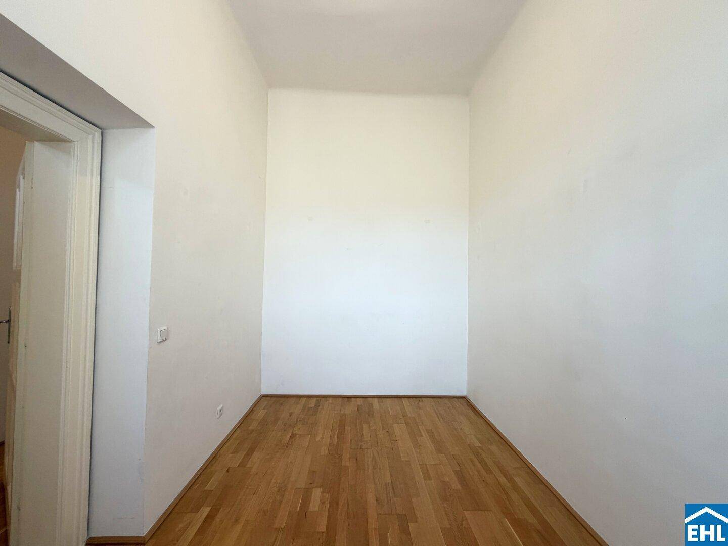 Leerer Raum mit Holzdielenboden und offenem Zugang zu einem anderen Bereich.