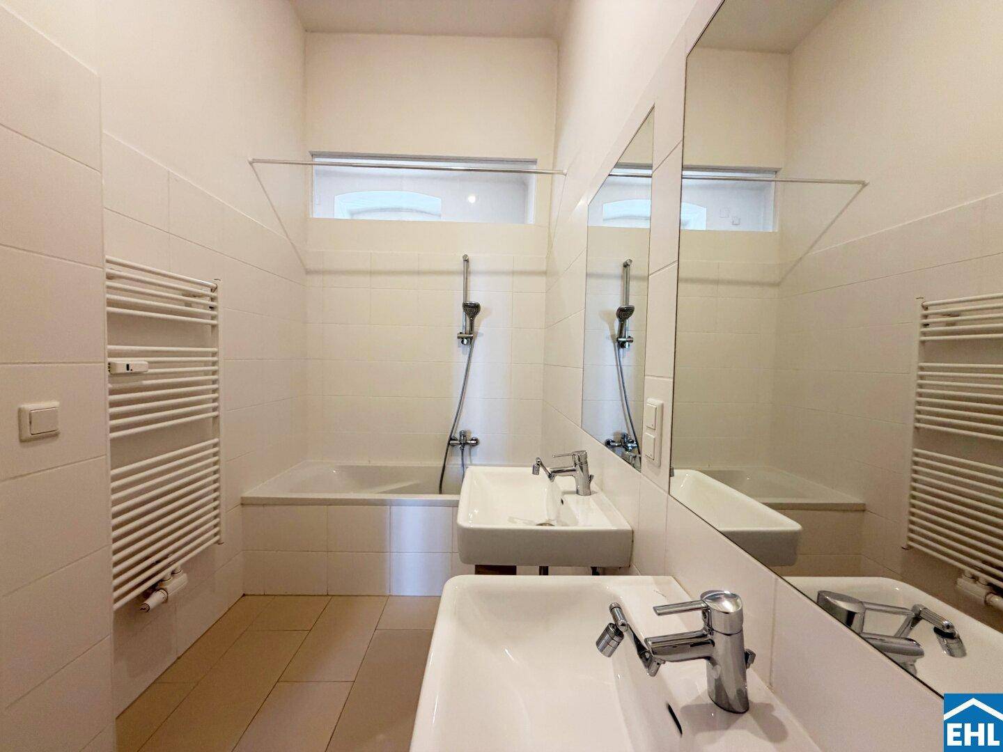 Modernes Badezimmer mit zwei Waschbecken, Badewanne mit Dusche und Handtuchheizkörper.
