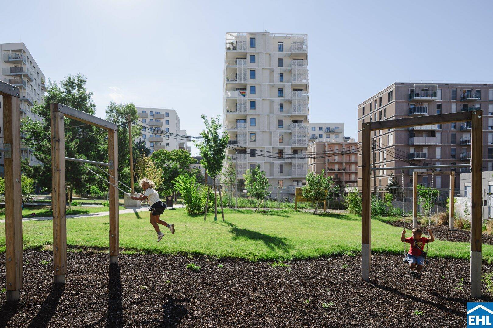 Spielplatz mit Schaukeln und Kindern, umgeben von modernen Wohngebäuden.