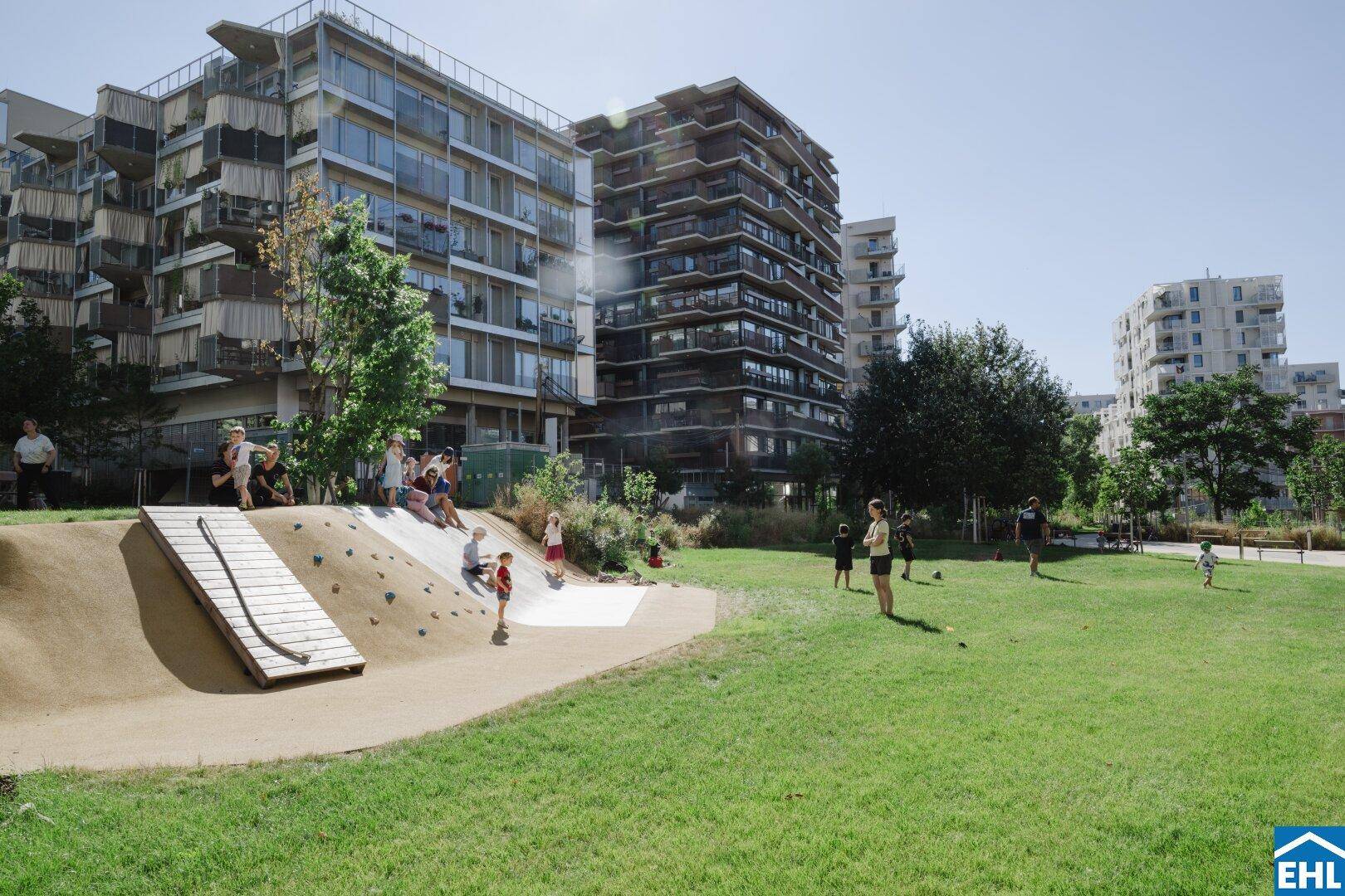 Moderner Spielplatz mit Kletterhügel und Rutsche, umgeben von Wohngebäuden.