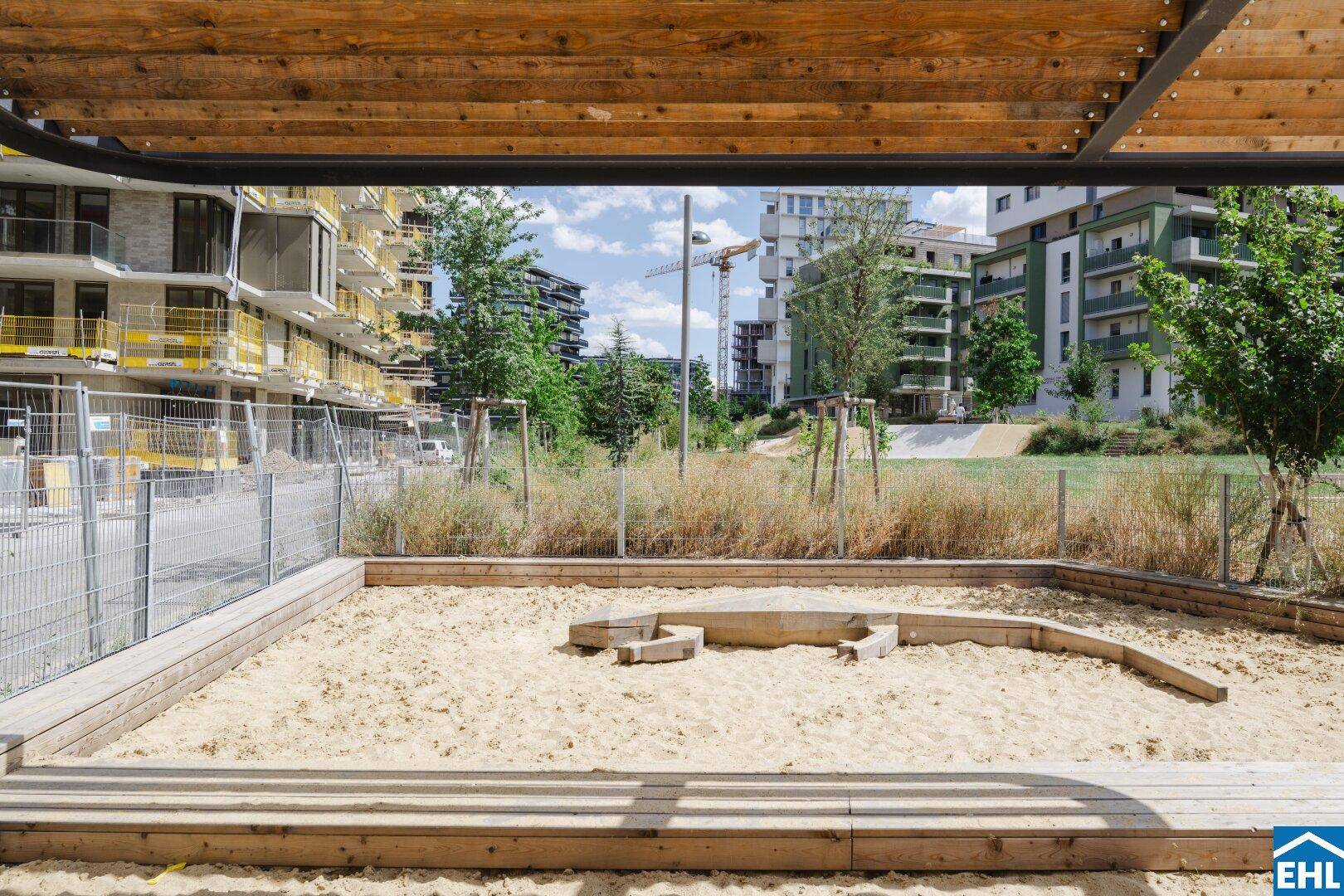Sandkasten unter einer Holzpergola, Teil eines Spielbereichs in einer neuen Wohnsiedlung.