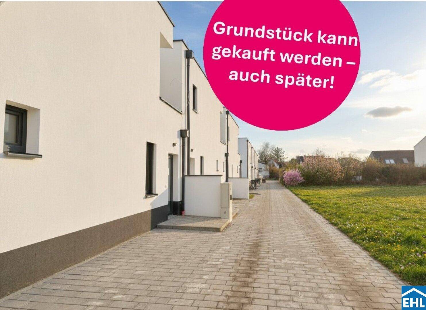 Moderne Reihenhäuser mit weißer Fassade und gepflastertem Zugangsweg, umgeben von Grünflächen unter sonnigem Himmel.
